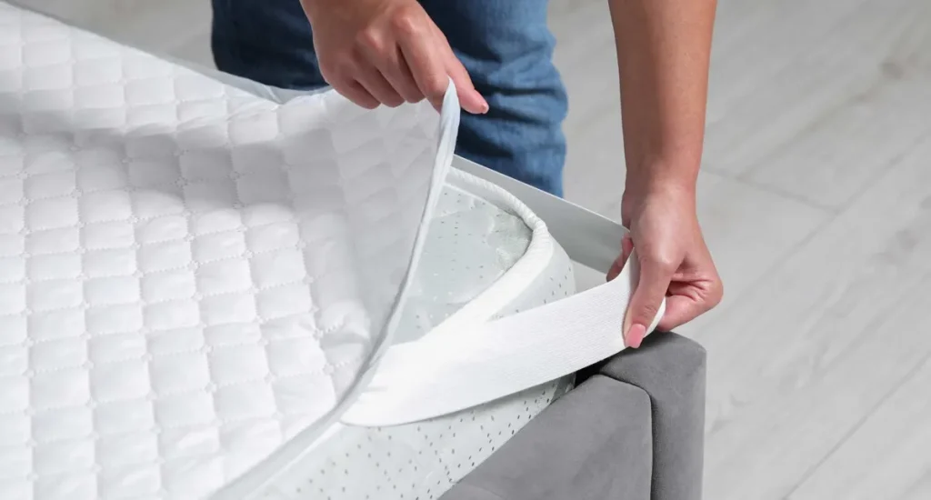 Personne installant un protège-matelas blanc sur un lit.