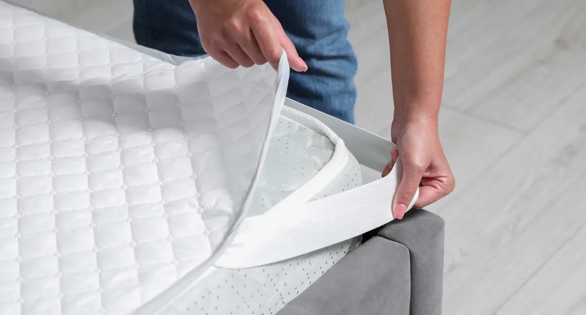 Personne installant un protège-matelas blanc sur un lit.